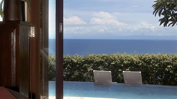 A room with a view of the ocean, a pool, and a chair with a red cushion. - Blue Point Resort and Spa (Pecatu)