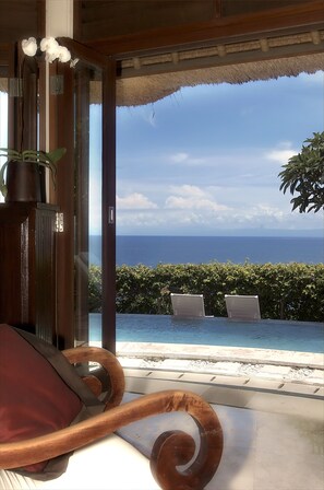 A room with a view of the ocean, a pool, and a chair with a red cushion. - Blue Point Resort and Spa (Pecatu)