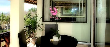 En balkon med et rundt bord, stole og krukker med planter.