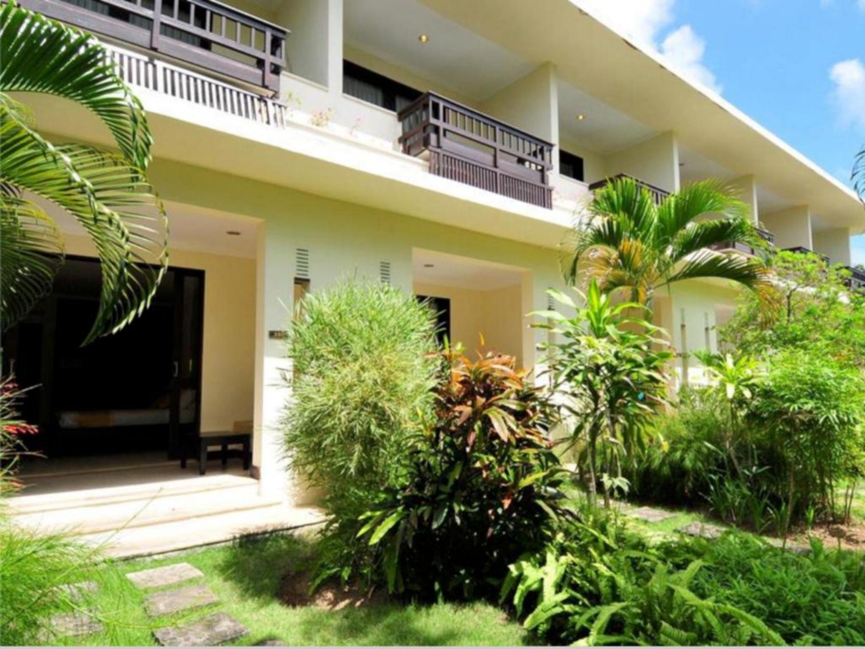 A two-story building with a balcony on the upper floor, surrounded by lush greenery and a well-maintained garden.