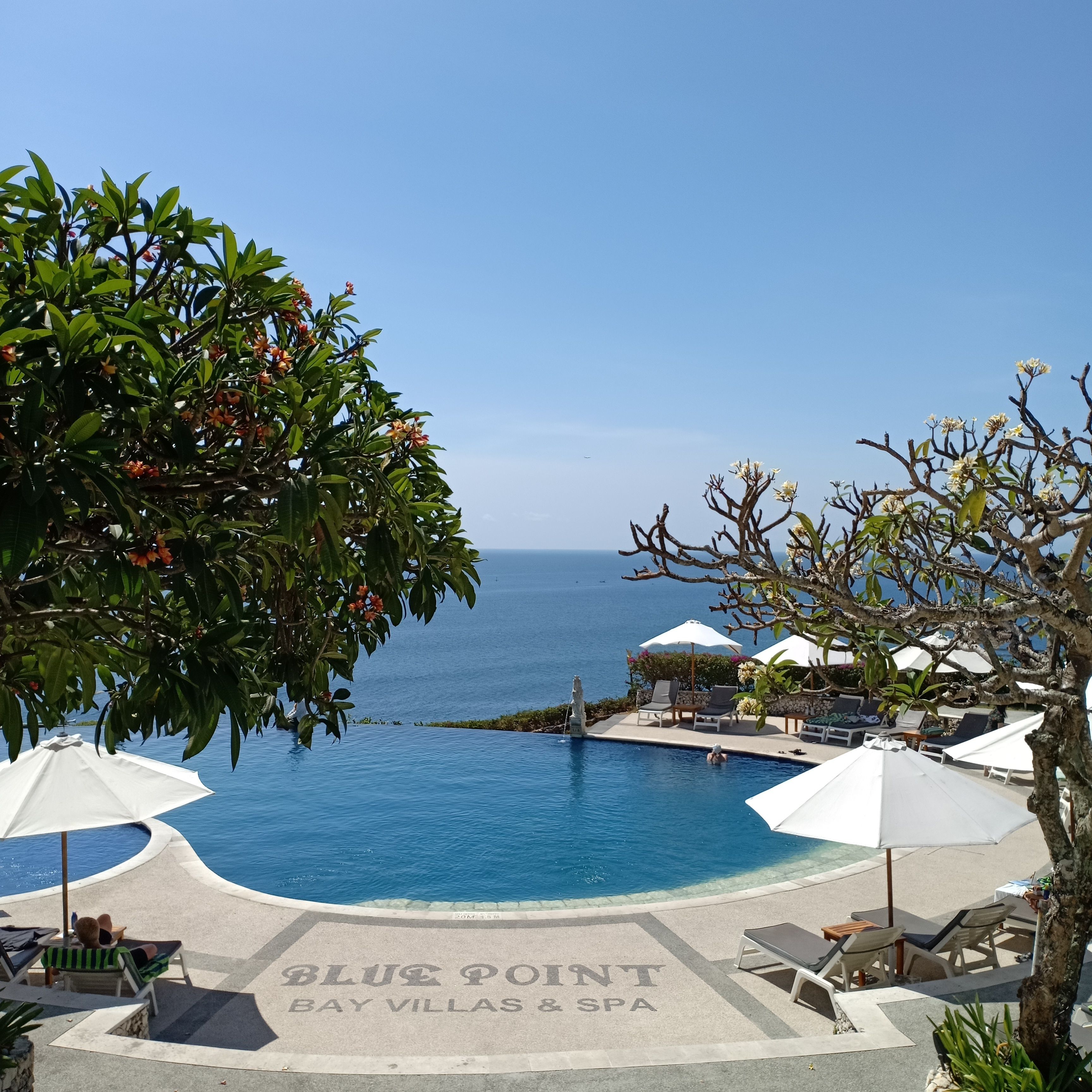 Zona de piscina con sillas de descanso y sombrillas, vista despejada al océano, y un cartel que dice "BLUE POINT BAY VILLAS & SPA".