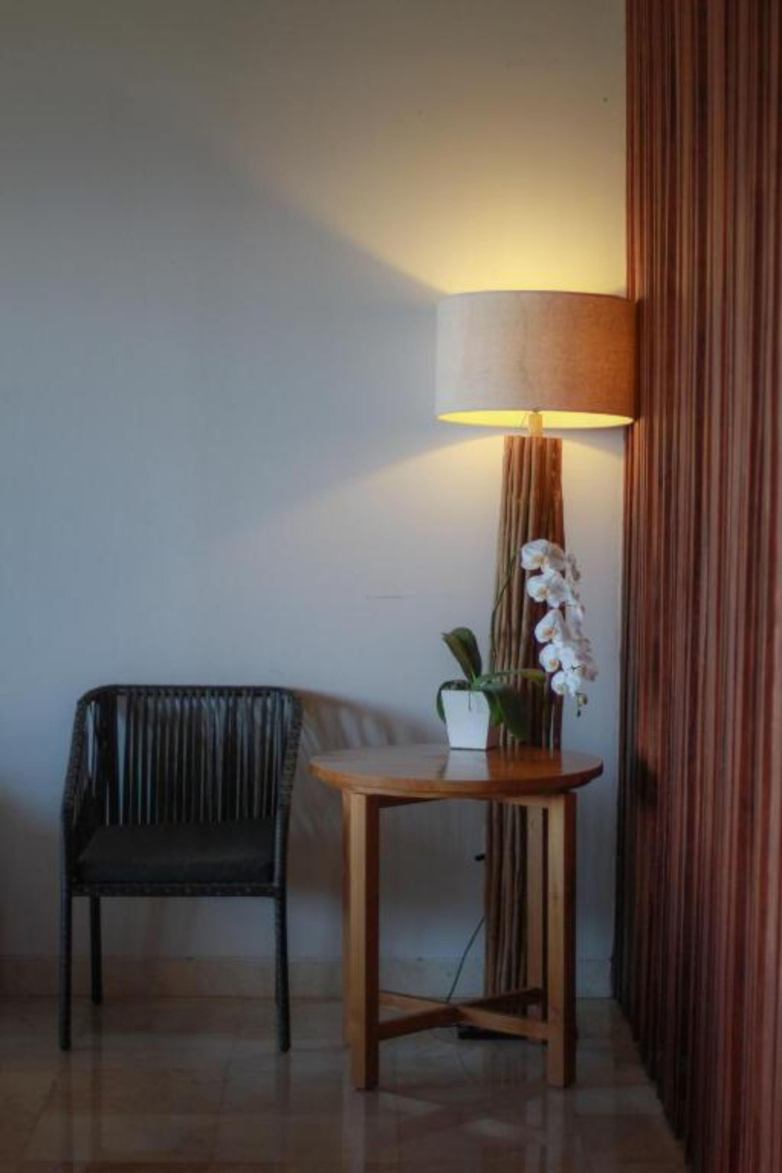 A corner with a black chair, a small wooden table with a lamp, and a potted orchid.