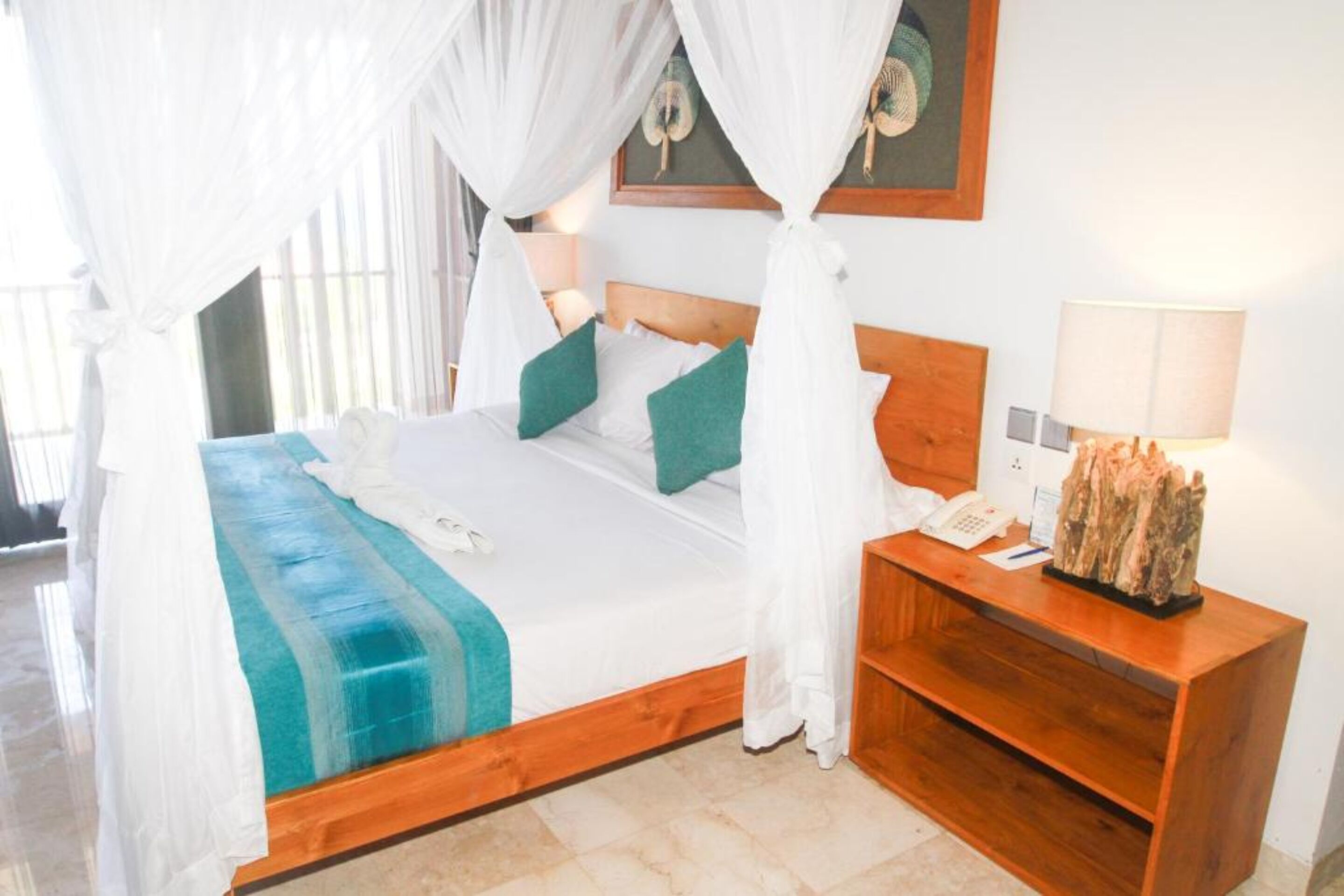 A bed with a canopy, a wooden nightstand, a telephone, and a decorative item on the nightstand.