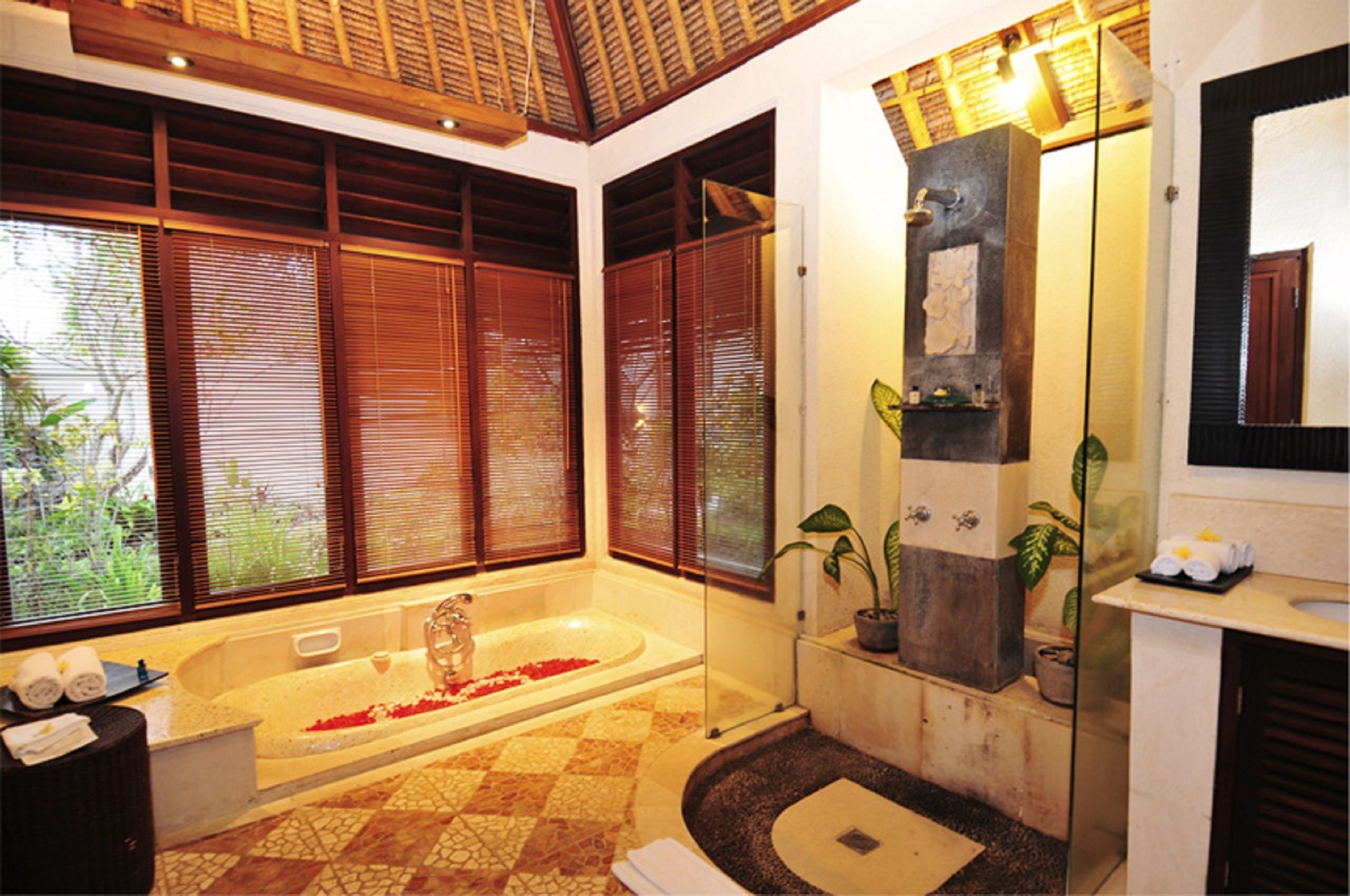 A bathroom with a large bathtub, a sink, and a mirror. There are potted plants and a shower area.