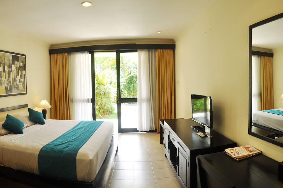 A hotel room with a bed, a desk with a TV, a large window with curtains, and a painting on the wall.
