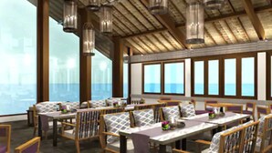 A restaurant with high ceilings, exposed wooden beams, and large windows offering a view of the sea. Tables are set with chairs, and hanging light fixtures are visible. - Blue Point Resort and Spa (Pecatu)