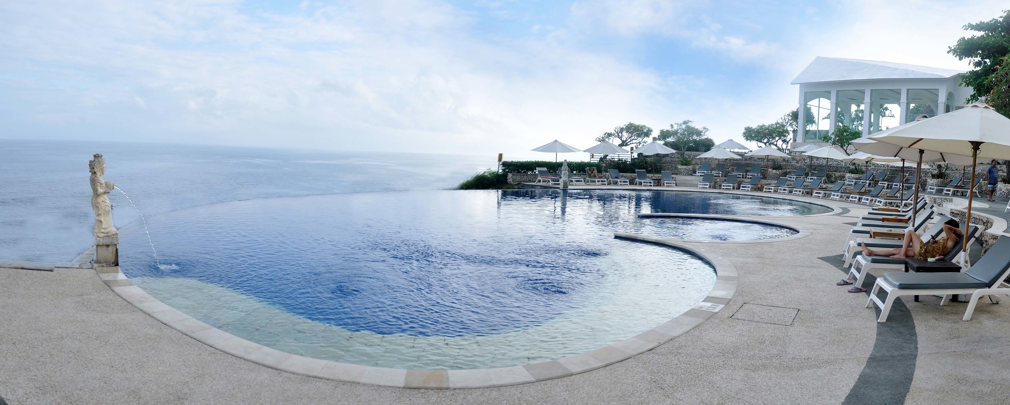 Une piscine à l’eau claire, des chaises longues, des parasols et une vue sur la mer.