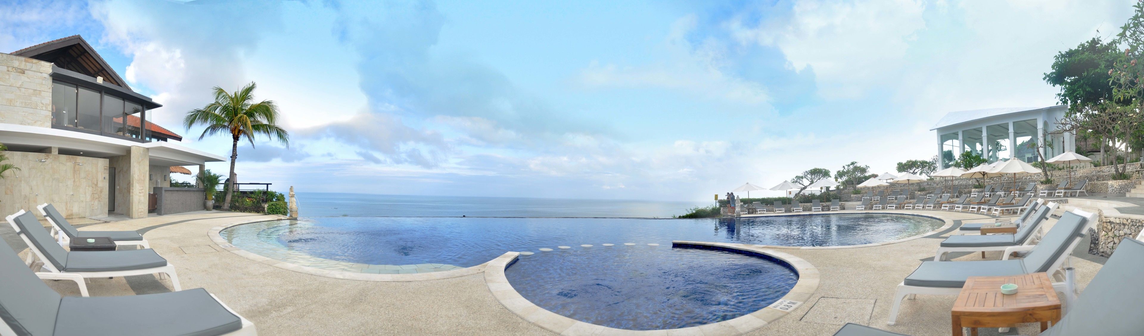A pool area with lounge chairs and a view of the ocean.