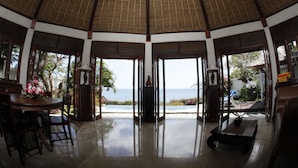 A spacious room with a high ceiling, a dining area with a table and chairs, and a view of the ocean. - Blue Point Resort and Spa (Pecatu)