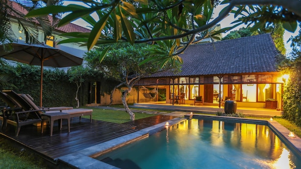 A pool area with a wooden deck, lounge chairs, and a hanging chair. - Villa Coco (Seminyak)