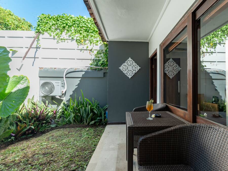 Un patio con mesa y sillas de mimbre, un adorno de pared y un jardín con diversas plantas.
