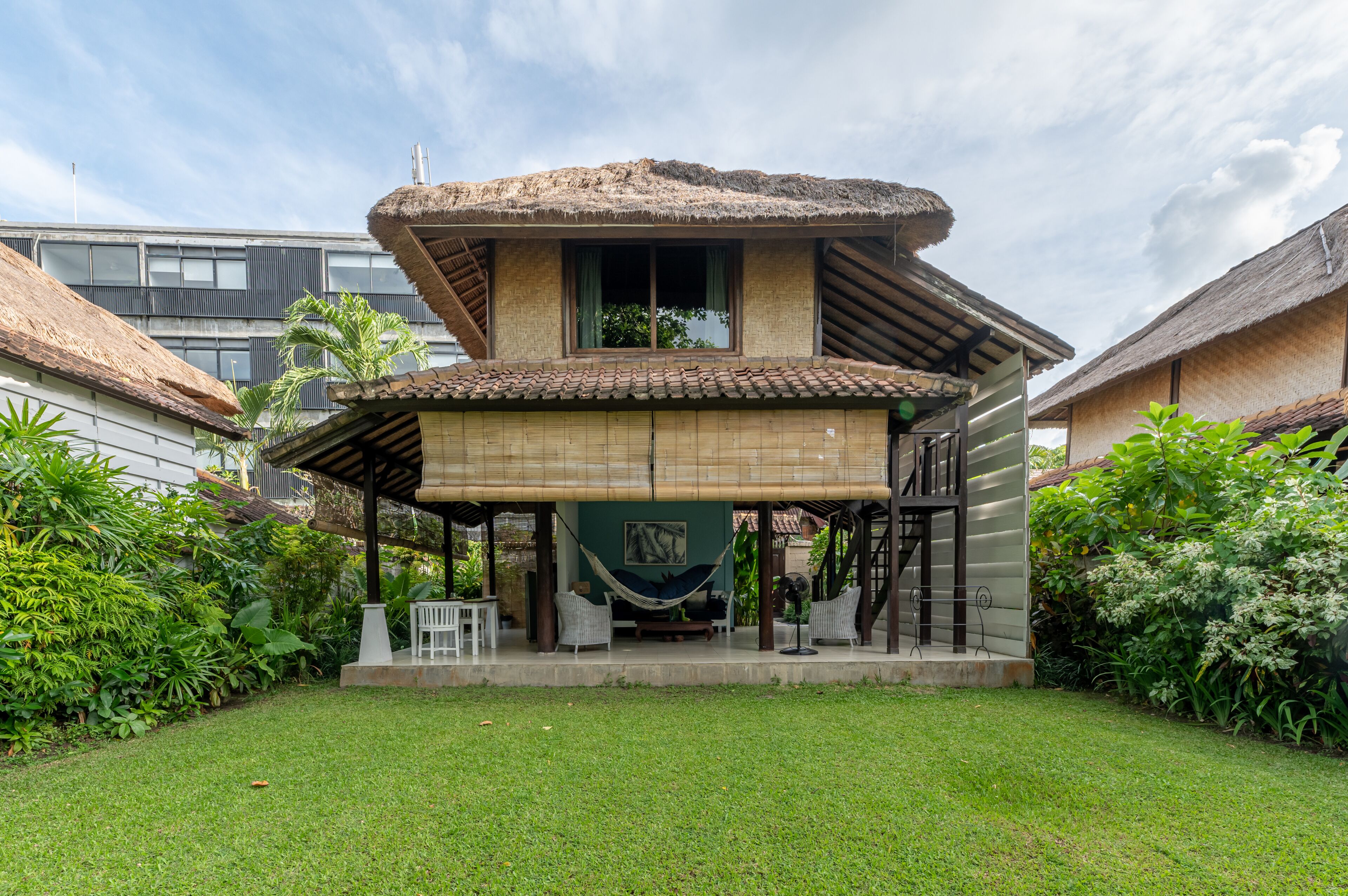 A house with a thatched roof, a hammock, and a small porch area with wicker furniture.