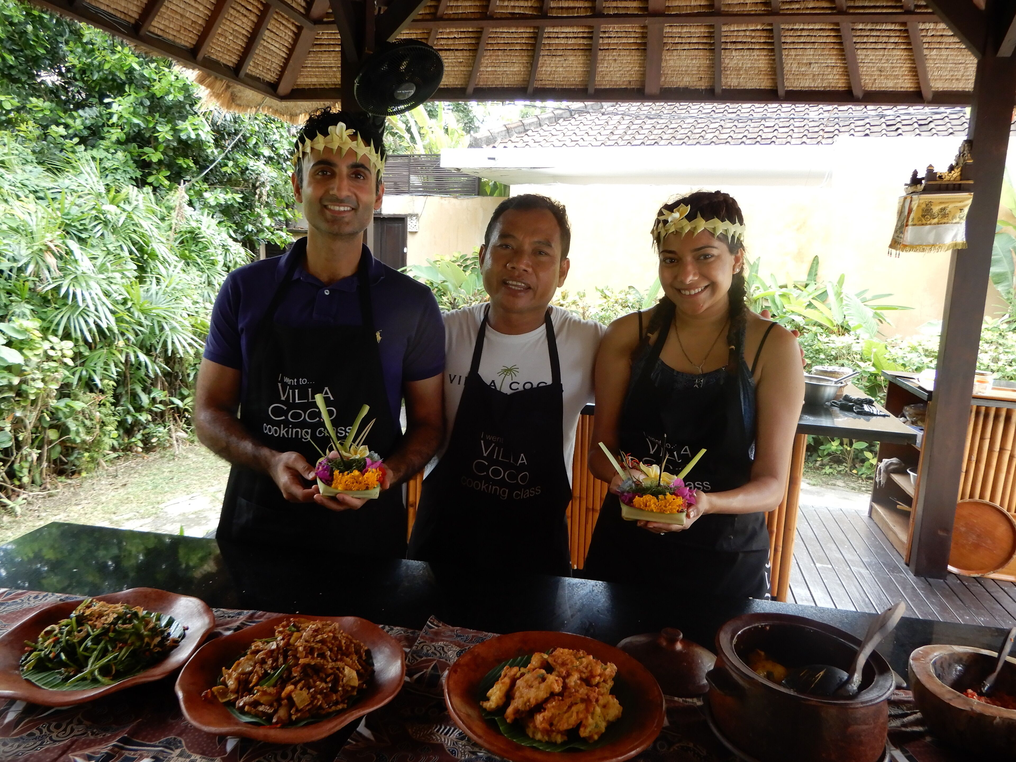 Three people standing in a covered outdoor area with tables displaying food dishes.