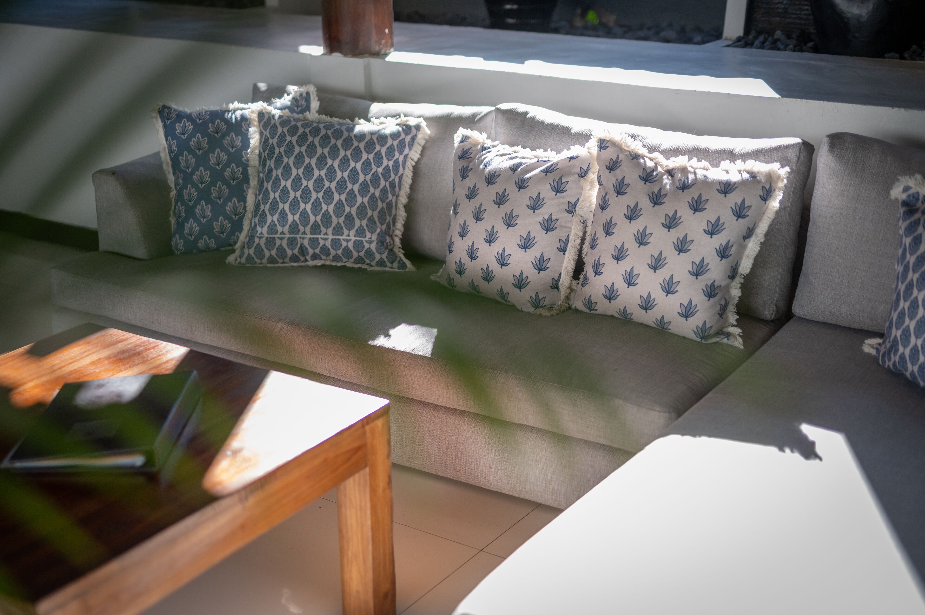 A modern outdoor seating area with a sofa and cushions, a wooden table, and a view of the outdoors.