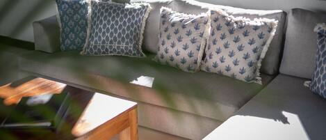 A modern outdoor seating area with a sofa and cushions, a wooden table, and a view of the outdoors.