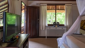 A room with a wooden ceiling, a bed with white bedding, a TV on a wooden cabinet, and a window with curtains. - Villa Coco (Seminyak)