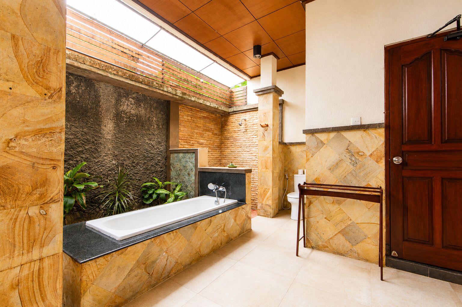A modern bathroom with a freestanding bathtub, stone walls, and a wooden door.