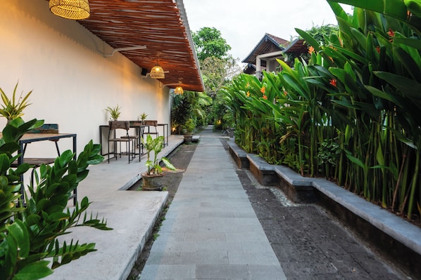 A pathway flanked by lush greenery and a wooden pergola with hanging lights.