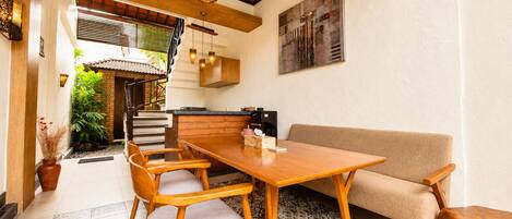 A dining area with a wooden table and chairs, a sofa, and a kitchen in the background.