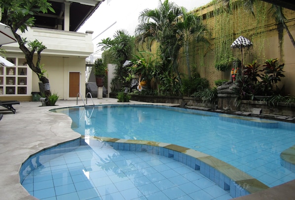 Una piscina con bordes azulejados, rodeada de plantas en macetas y una zona de estar cubierta.