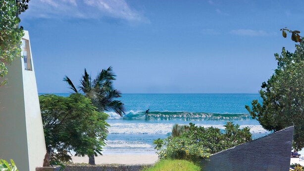 A beach view with a clear sky, palm trees, and a person surfing. - AlamKulKul Boutique Resort Kuta Bali (Legian)