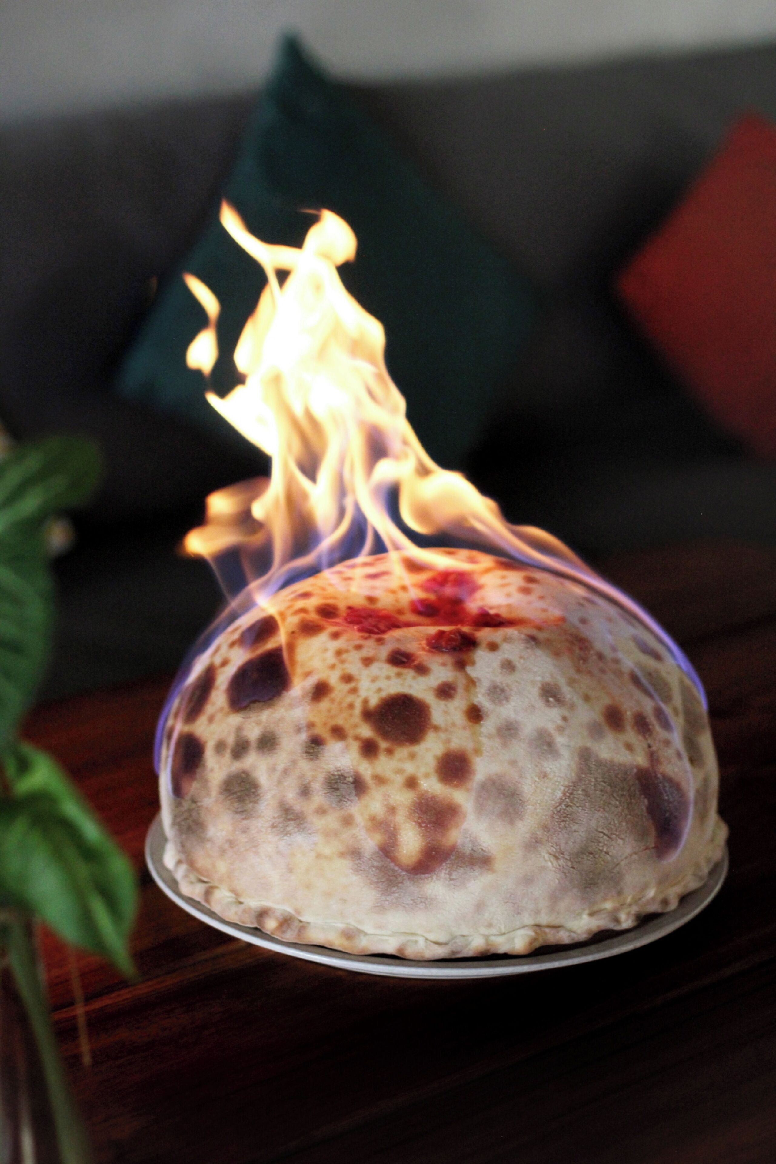 A flatbread with flames on a plate, placed on a wooden table with a couch and cushions in the background.