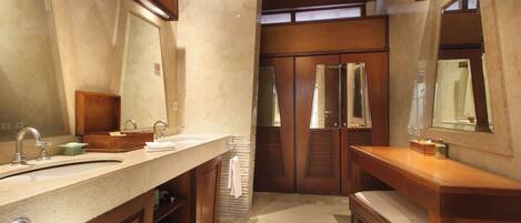 Un baño con un lavamanos grande, espejo, tocador de madera, banco y piso de baldosas.