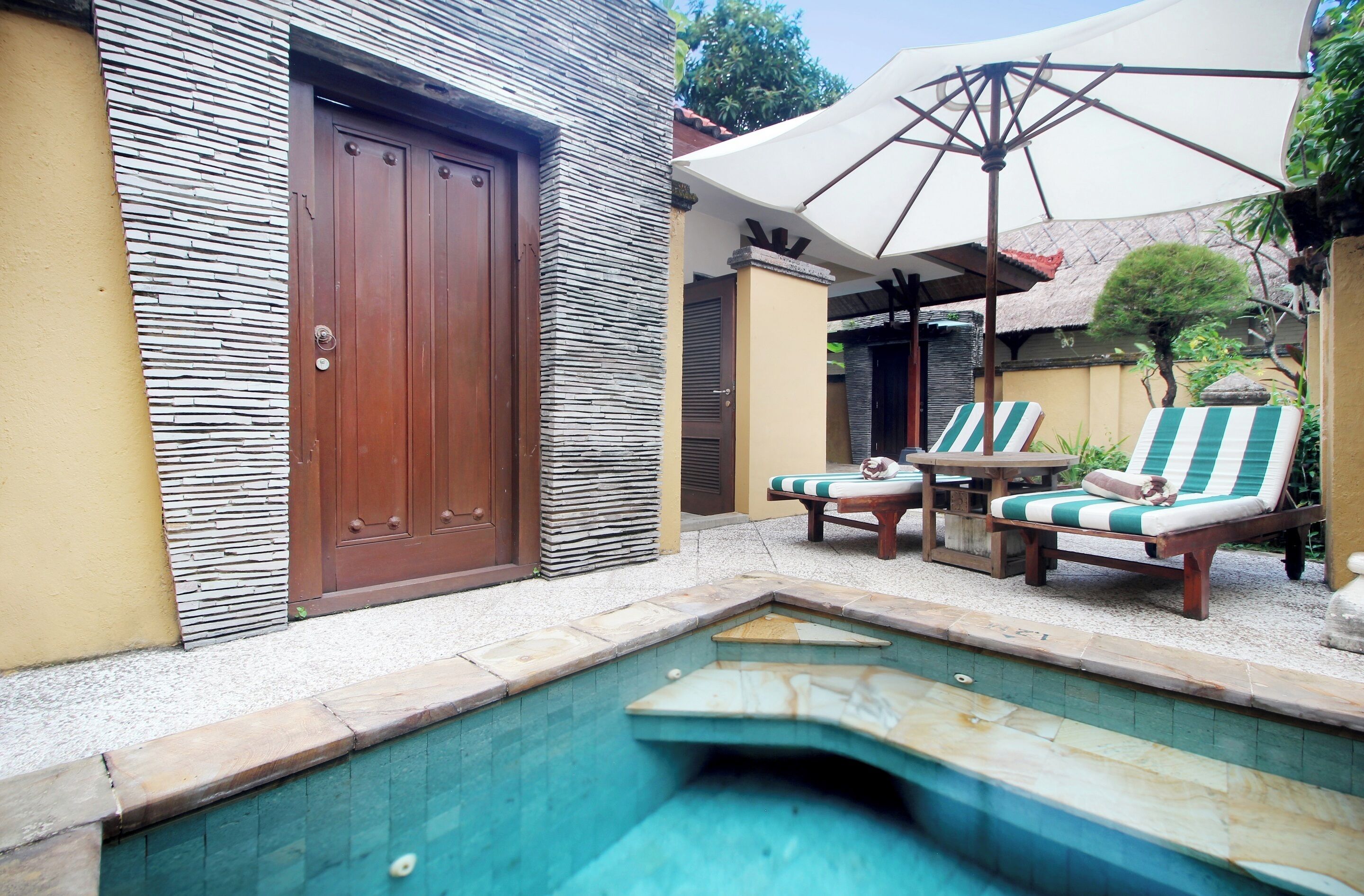 A pool area with two lounge chairs, a table, and an umbrella.