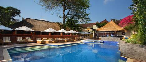 Une piscine entourée de bâtiments et d’arbres, avec des chaises longues et des parasols.