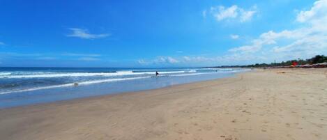 A wide sandy beach with footprints, a clear blue sky, and the ocean in the background.