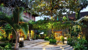 A courtyard with a stone staircase leading to a building entrance, surrounded by lush greenery and outdoor seating areas. - AlamKulKul Boutique Resort Kuta Bali (Legian)