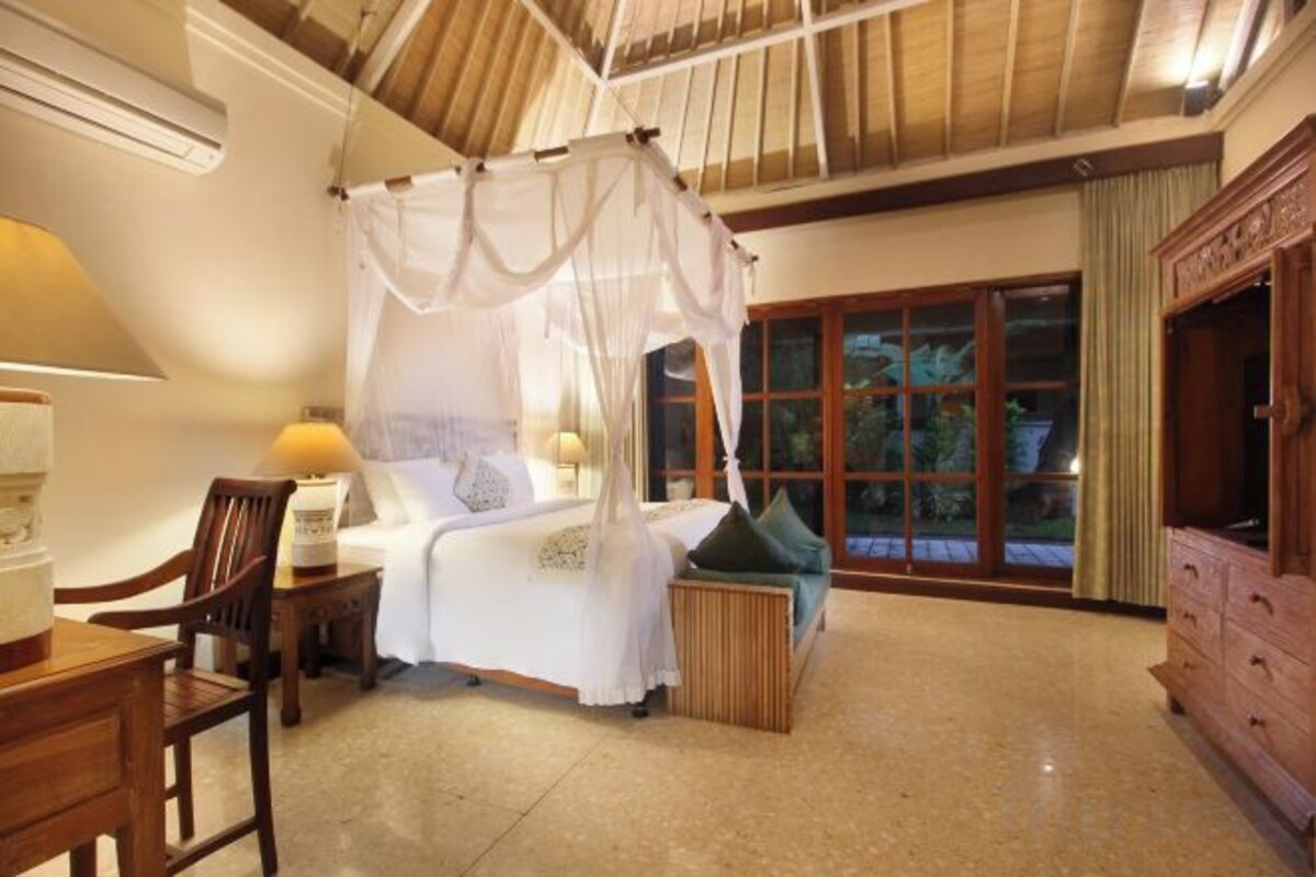 A bedroom with a canopy bed, a wooden nightstand, a chair, a dresser, and a large window with a view.