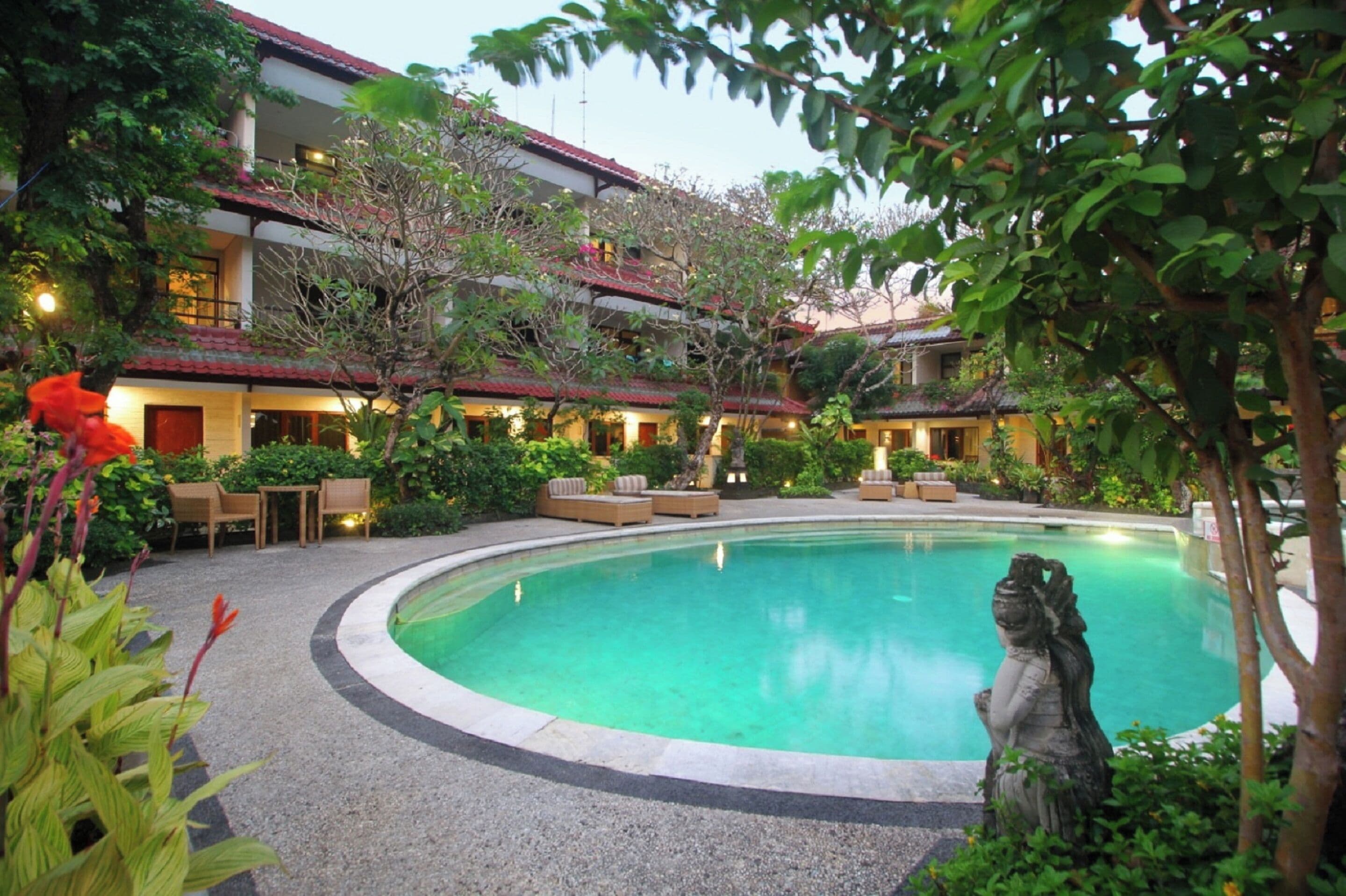 A hotel courtyard with a swimming pool, outdoor seating, and lush greenery.