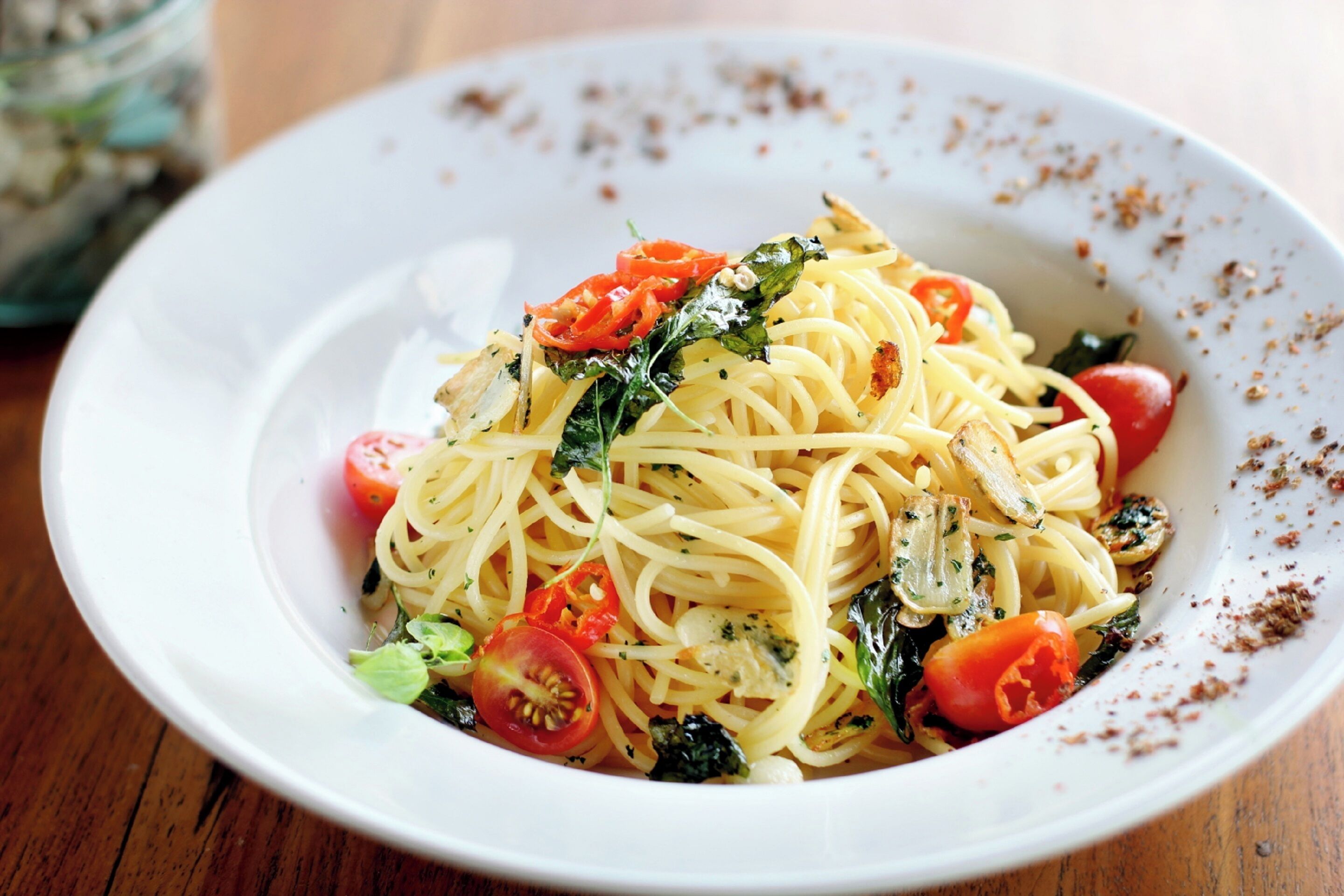 A white plate with spaghetti, cherry tomatoes, and greens.