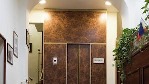 L’entrée d’un hôtel, avec un escalier en marbre, un paillasson sur lequel est inscrit le nom « Hôtel Strombali » et une pancarte « Bienvenidos ».