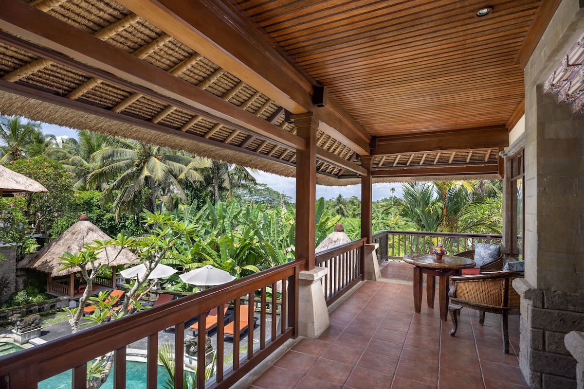 A covered outdoor area with a wooden ceiling, a pool, and a view of lush greenery and palm trees.