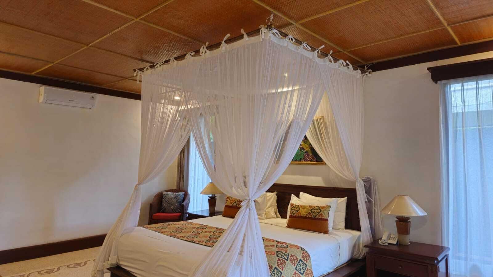 Une chambre à coucher avec un lit à baldaquin, une table de chevet avec une lampe et un fauteuil avec un coussin.