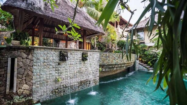 A resort with a stone wall, a pool with water features, and thatched-roof buildings. - Kori Ubud Resort (Ubud)