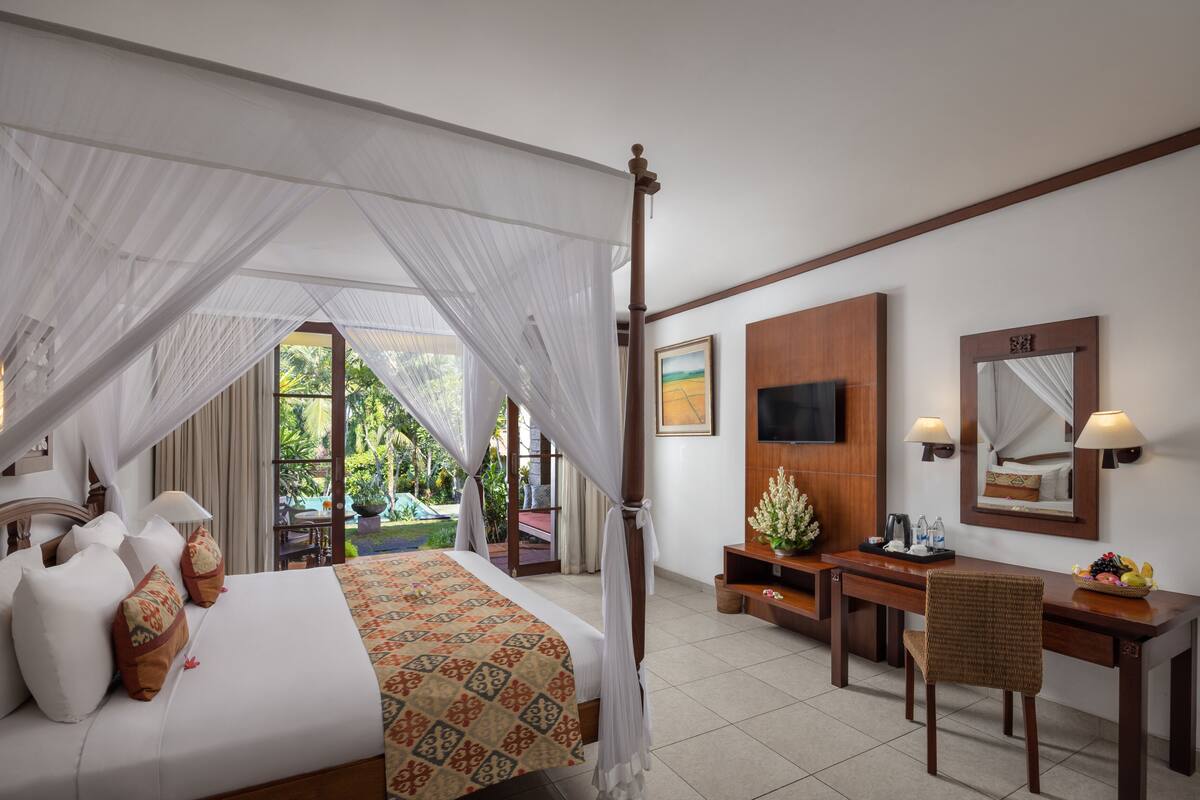 A four-poster bed with a canopy, a desk with a chair, a television, and a mirror.