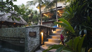 A stone staircase leading to a building with a thatched roof, surrounded by lush tropical vegetation. - Kori Ubud Resort (Ubud)