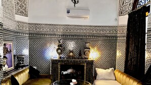 A room with a checkered floor, a sofa, a table with a red cushion, and a fireplace. - Riad Damia Suite &Spa (Fes)