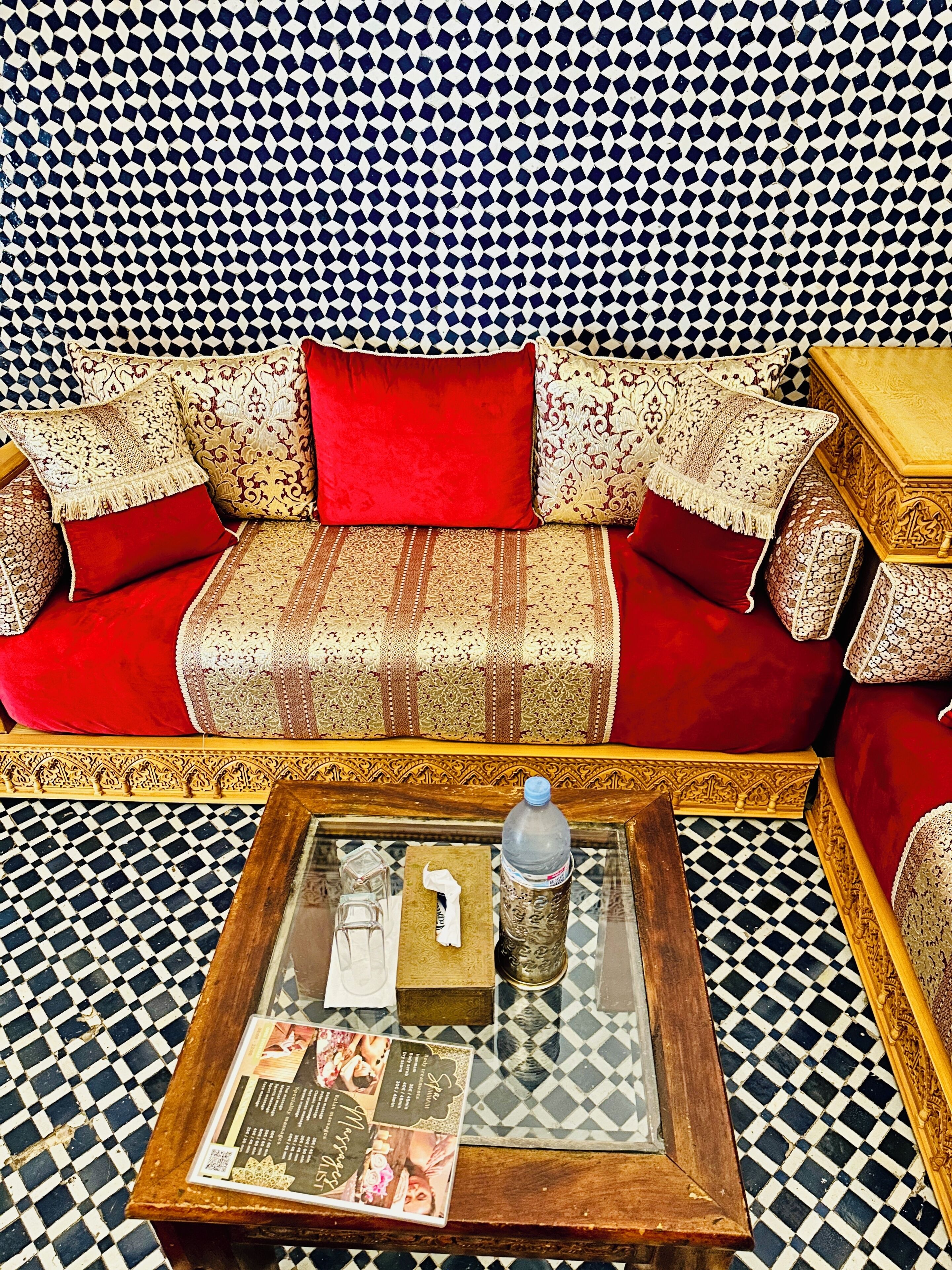 Um quarto com piso xadrez, sofá com almofadas estampadas, mesa de centro com uma revista e uma parede decorativa.
