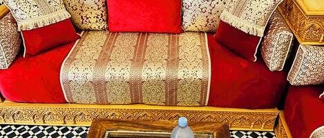 Um quarto com piso xadrez, sofá com almofadas estampadas, mesa de centro com uma revista e uma parede decorativa.
