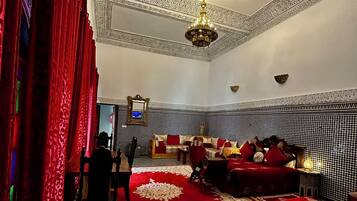 Una habitación con piso a cuadros, cortinas rojas, candelabro, sofá y cama con ropa de cama roja.