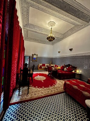 A room with a checkered floor, red curtains, a chandelier, a sofa, and a bed with red bedding. - Riad Damia Suite &Spa (Fes)