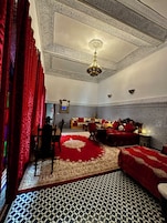 Una habitación con piso a cuadros, cortinas rojas, candelabro, sofá y cama con ropa de cama roja.