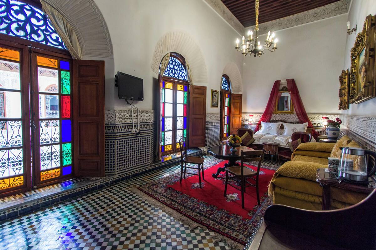 A room with a checkered floor, wooden furniture, a red carpet, and colorful stained glass windows.