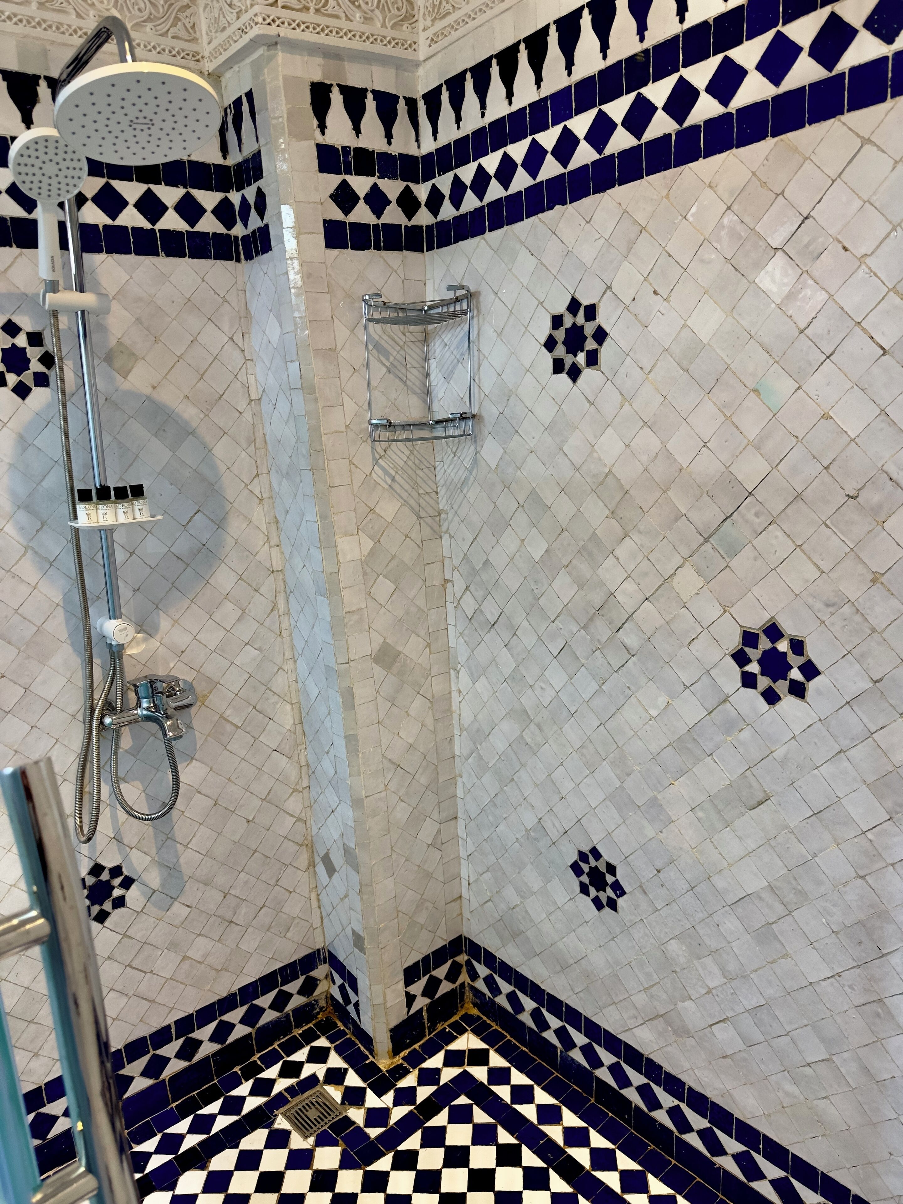 Un baño con piso a cuadros, ducha con cabezal de ducha manual y pared de azulejos con diseño geométrico.