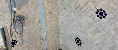 Un baño con piso a cuadros, ducha con cabezal de ducha manual y pared de azulejos con diseño geométrico.