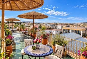 A rooftop terrace with outdoor seating, umbrellas, and potted plants.
